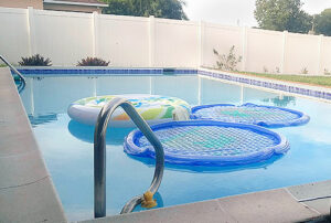 A pool in a fenced in yard has floating toys in it.
